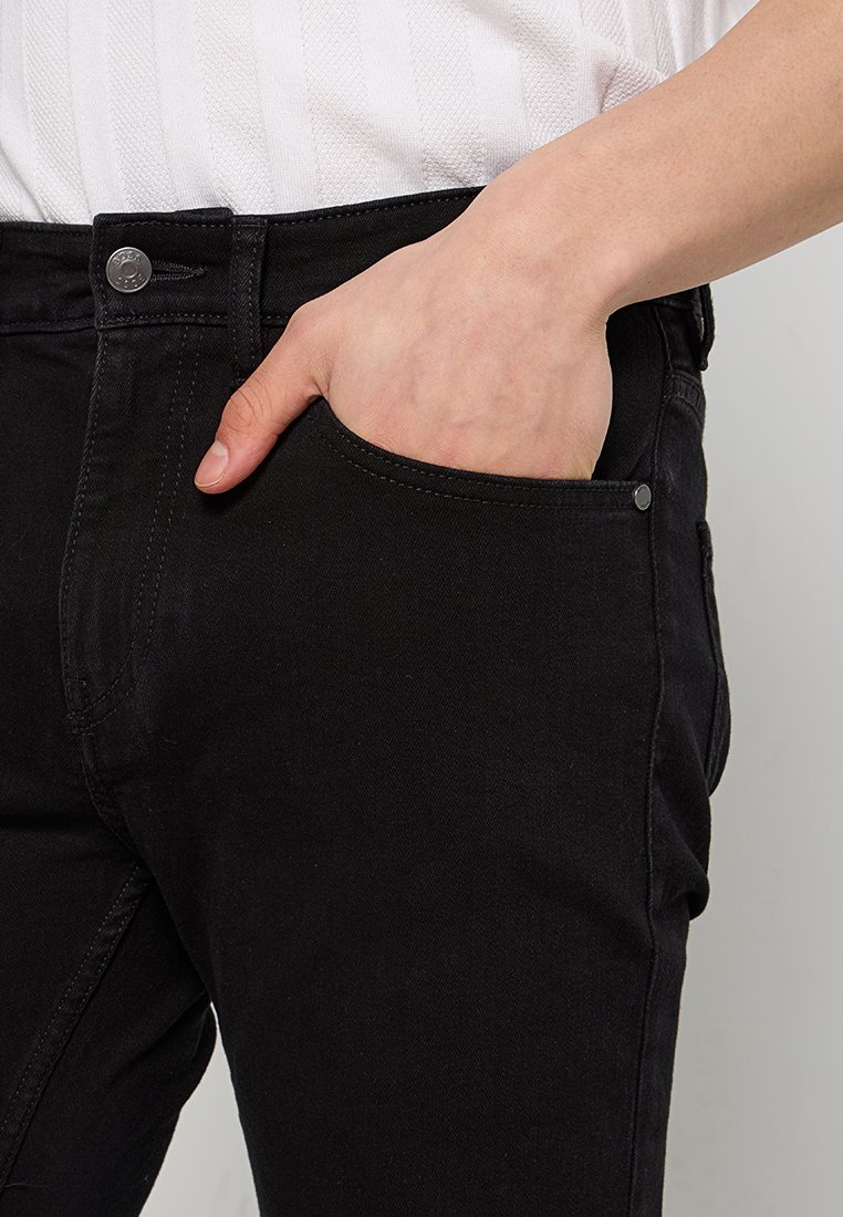 Jeans en denim noir avec une coupe droite, dotés d'une poche avant et de détails en métal à la taille. Tissu texturé, coupe décontractée.