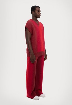 Rød strikket oversized ærmeløs top med V-hals, parret med brede røde bukser. Blød tekstur, gradientfarve og afslappet design.