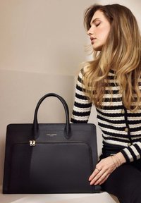 Schwarze Lederhandtasche mit strukturiertem Design, doppelten Tragegriffen, einer Vorderzippertasche und dezentem Logo. Die strukturierte Oberfläche ergänzt das Gesamterscheinungsbild.