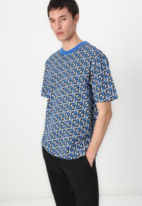 Kurzärmliges T-Shirt in Blau mit einem geometrischen Schwarz-Weiß-Muster, ausgestattet mit einem blauen Rundhals und lockerer Passform. Weicher Stoff.