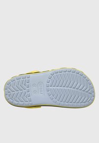 Żółte i czarne klompy z białą gumową podeszwą, wyposażone w teksturowany wzór bieżnika zapewniający przyczepność. Widoczne logo na podeszwie.