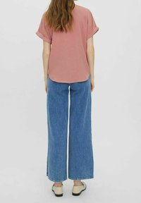 Tenue décontractée composée d'un haut rose à manches courtes et d'un jean bleu taille haute à jambes larges, avec manches retroussées et coupe ample.