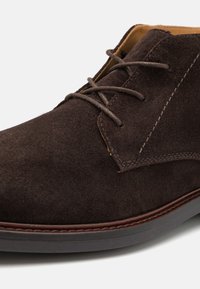 Brown suede chukka shoe featuring a rounded toe, brown laces, contrast stitching, and a low-profile rubber sole.