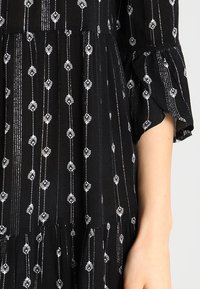 Schwarzes Kleid aus Stoff mit weißen geometrischen Mustern, Rüscheärmel und einem gestuften Design mit strukturierter Oberfläche.