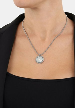 Collar de cadena de plata con un colgante circular que presenta un centro de piedra azul lisa y un borde grabado, lucido sobre una blusa oscura.