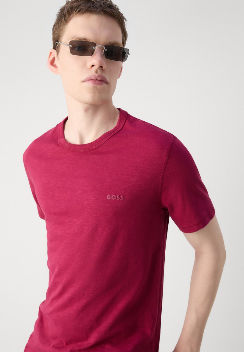 T-shirt à col rond bordeaux en tissu doux ; présente un logo "BOSS" subtil de la même couleur sur la poitrine ; texture lisse.