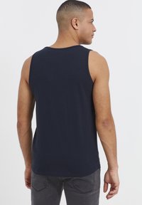 Marineblå ermeløs skjorte laget av bomull, med rund halsutskjæring, rett nederkant og glatt tekstur, brukt sammen med grå jeans.