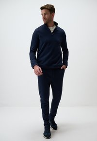 Sweat à capuche zippé bleu marine à manches longues, associé à un pantalon de jogging assorti. Tissu lisse et design ajusté avec poches et taille élastique.