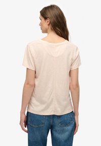 Maglietta rosa chiaro con maniche corte, scollo rotondo e una cucitura al centro del retro. Realizzata in tessuto morbido, abbinata a jeans di denim blu.