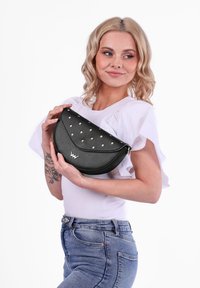 Černá kabelka z fauzní kůže s zakřiveným tvarem, zdobená růžově zlatými hroty. Zapínání na zip, s logem na přední straně.