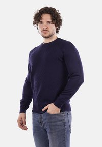 Maglione lavorato a maglia blu navy con un motivo testurizzato, scollatura rotonda e maniche lunghe, abbinato a jeans azzurri chiari.