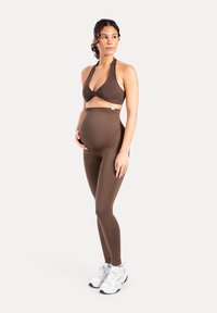 Brassière de sport marron pour femmes enceintes avec un design halter et un legging taille haute assorti, tous deux en matière lisse et extensible. Baskets blanches incluses.