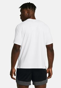 Camiseta blanca de manga corta con cuello redondo, textura suave y aberturas laterales, combinada con pantalones cortos de malla negros con dobladillo gris.