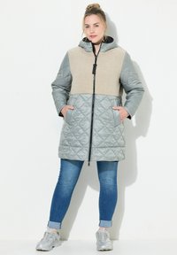 Gestepptes Jacket mit einem grauen, gepolsterten Unterteil und einem oberen Abschnitt aus beigem, weich strukturiertem Material. Verfügt über eine Kapuze und Seitentaschen, mit einem Reißverschluss vorne.