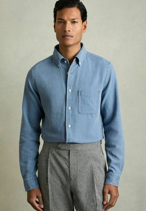 Camisa de botones azul claro con cuello, mangas largas y bolsillo delantero. Combinada con pantalones de talle alto grises con textura.