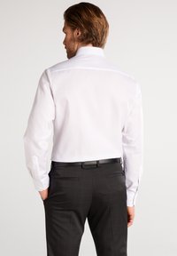 Weißes Hemd mit spitzem Kragen, langen Ärmeln und Knopfmanschetten, kombiniert mit schwarz-gestreiften Hosen und einem schwarzen Gürtel.