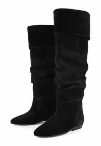 Bottes en suède noir au-dessus du genou avec un design fluide, bout pointu et petit talon empilé. Présente des coutures visibles et une texture douce.