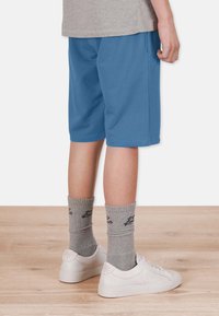 Blå bomullsshorts, knälånga, med fickor. Grå ribbstickade strumpor med svart logotyp, använda med vita sneakers. Enkel grå t-shirt synlig ovanför shortsen.