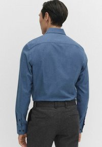 Męska koszula z długim rękawem w niebieskim kolorze, o gładkiej fakturze, z kołnierzem typu pointed i mankietami na guziki. Dopasowany krój z detalem w postaci yoke na plecach.