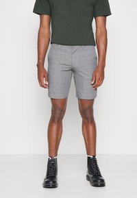 Shorts gris à carreaux avec une coupe ajustée, tissu léger, poches latérales, associés à des bottes noires à lacets et un t-shirt noir.