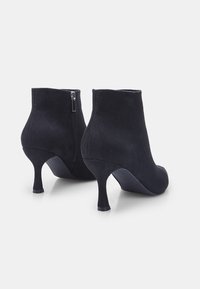 Bottes noires en daim à la cheville avec une silhouette effilée, fermeture éclair sur le côté et des talons de 5 cm, présentant une texture lisse et un design minimaliste.