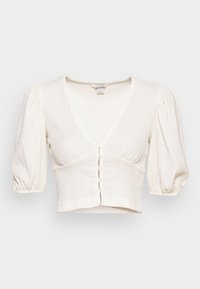 Blusa bianca corta con scollatura a V, maniche a sbuffo e chiusura frontale con bottoni. Il tessuto testurizzato aggiunge un dettaglio sottile.