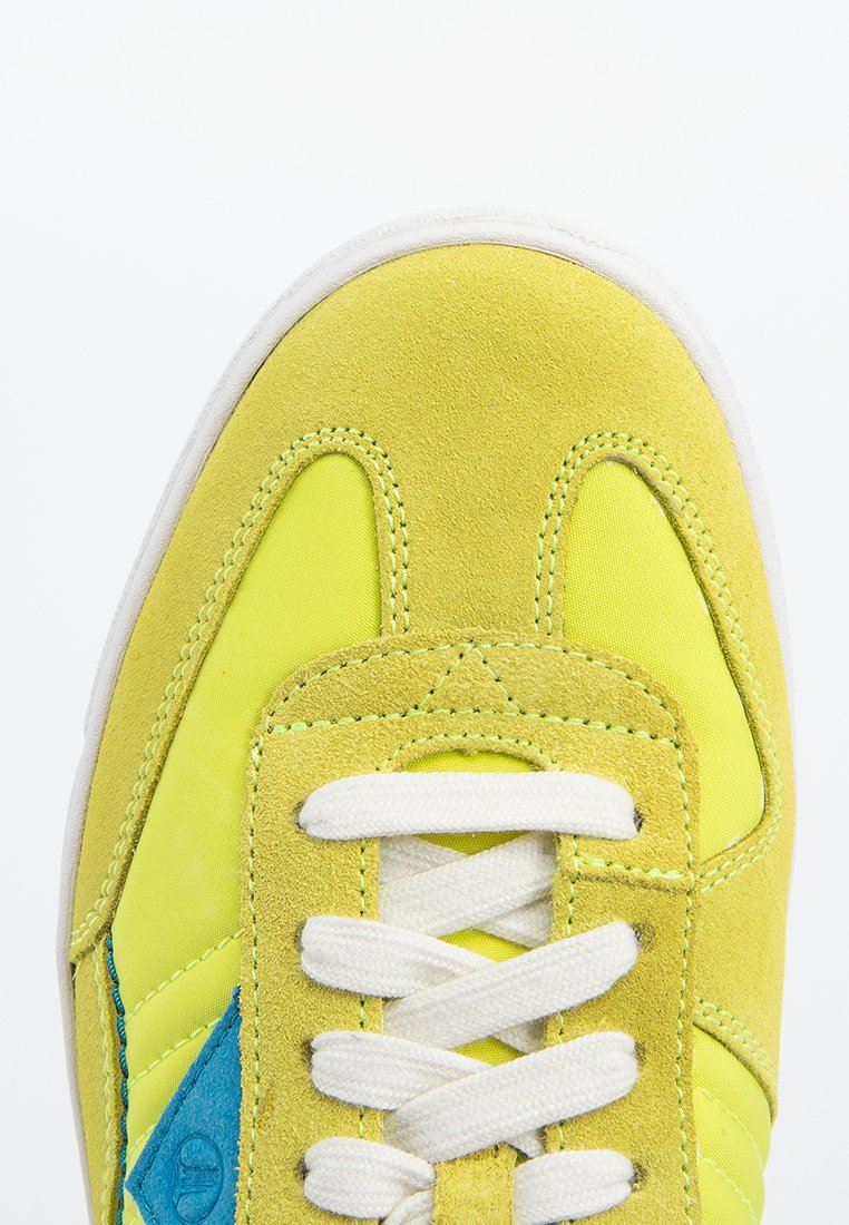 Zapatillas amarillas con materiales de ante y sintéticos, que presentan un triángulo de acento azul, cordones blancos y un acabado texturizado en la parte superior.