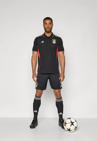 Meeste must jalgpallivorm punaste aktsentidega, millel tikitud embleem, kolm valget triipu varrukatel ja sokkidel ning mustad saapad.