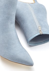 Botas de tobillo con punta afilada en tejido azul claro con un acabado texturizado. Presentan una cremallera lateral y un ribete azul liso a lo largo de la abertura.