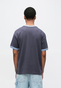 Βαμβακερό μπλουζάκι σε σκούρο γκρι χρώμα με ανοιχτού γαλάζιου ριμπ περιμετρικά στο λαιμό και στα μανίκια. Διαθέτει άνετη εφαρμογή και λεία υφή.