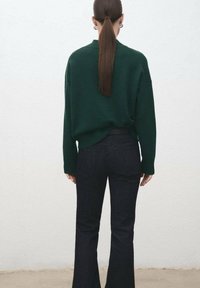 Maglione verde oversize realizzato in morbido materiale, abbinato a jeans a campana scuri a vita alta. Design semplice con dettagli a coste.