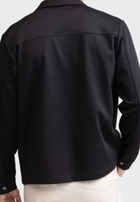Zwart, langarm shirt van gladde stof, met een kraag en knopenmanchetten, een gebogen zoom en een effen achterzijde.