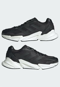 Zapatillas deportivas negras con parte superior de malla, tres franjas oscuras y suela texturizada blanca. Presenta un collar acolchado y cierre con cordones.