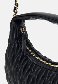 Sac à main en cuir noir avec une texture matelassée, doté d'une fermeture éclair dorée et d'accents en chaîne. Le design présente une forme courbée et une anse souple.