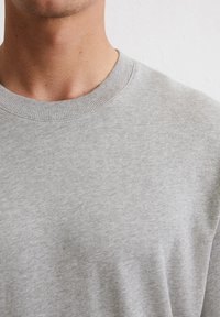 Grijze ronde hals sweatshirt gemaakt van een zachte, gladde stof. Het heeft een geribbelde halslijn en een effen textuur zonder patronen of accenten.