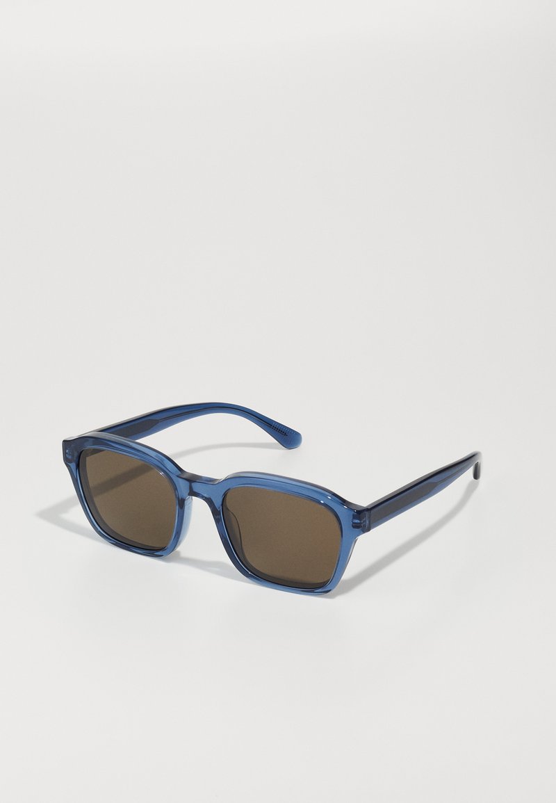 Ochelari de soare din plastic transparent albastru, cu rame pătrate și lentile de culoare maro închis. Brațe drepte cu detalii texturate, evidențiind un design modern.