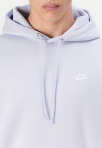 Hoodie Nike de cor roxa claro com cordão, textura suave e logotipo bordado no peito. Design casual, tecido de peso médio.