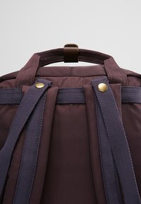 Dark purple backpack with a textured fabric, featuring a top handle and dual straps. Metal accents include gold buttons for added detail.