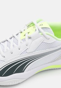 Zapatilla blanca con paneles de malla, acentos en verde neón y una raya en gris oscuro. Cuenta con diseño de cordones y un cuello acolchado para mayor comodidad.