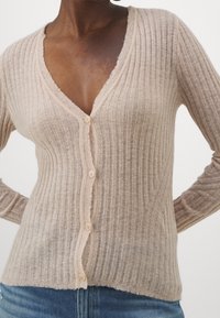 Cardigan beige côtelé ajusté en matière douce, avec un col en V profond, six boutons sur le devant et des détails de texture subtils.