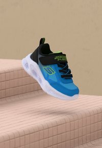 Blaue und schwarze Skechers S-Lights Sneaker mit weißer Sohle, die über beige geflieste Treppen schweben.