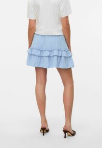 Jupe évasée bleu clair avec des volants au niveau de l'ourlet, fabriquée en tissu texturé. Associée à un haut blanc et des talons ouverts bruns.