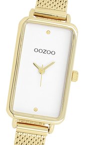 Montre rectangulaire dorée avec un cadran blanc, au design minimaliste, bracelet en maille et deux aiguilles dorées. Arrière-plan portant le nom de la marque "OOZOO".