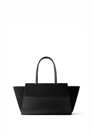 Sac à main trapézoïdal noir avec rabat en cuir suédé, deux poignées supérieures et côtés ailés, posé sur fond blanc.
