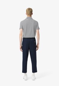 Polo rayé avec un col, associé à un pantalon bleu marine. Le pantalon dispose d'une poche arrière et d'un logo Lacoste. Chaussures : chaussettes et chaussures blanches.