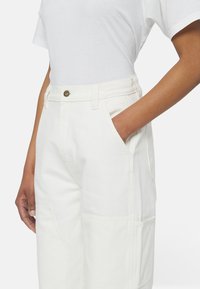 Vita, vida byxor i tjock bomull med hög midja, sidofickor och metallknäppe fram.