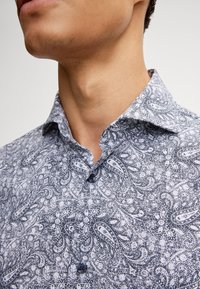Camicia con colletto e bottoni, caratterizzata da un motivo paisley blu navy su sfondo bianco, realizzata in tessuto strutturato e con vestibilità su misura.