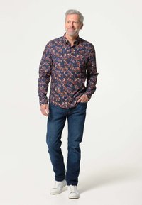 Een shirt met lange mouwen op een marineblauwe achtergrond met een kleurrijk bladerenpatroon. Draag het met donkere jeans en witte sneakers.