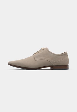 Beige lace-up shoes made of soft suede, featuring a pointed toe, minimal stitching, and a wooden heel. Smooth texture and simple design.