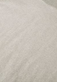 Gros plan sur un tissu tricoté côtelé doux beige avec une texture verticale subtile et de légères ondulations sur la surface.